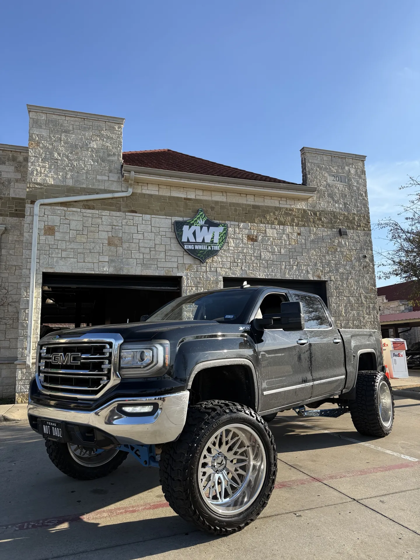 A lifted GMC Sierra on polished forged wheels outside the shop