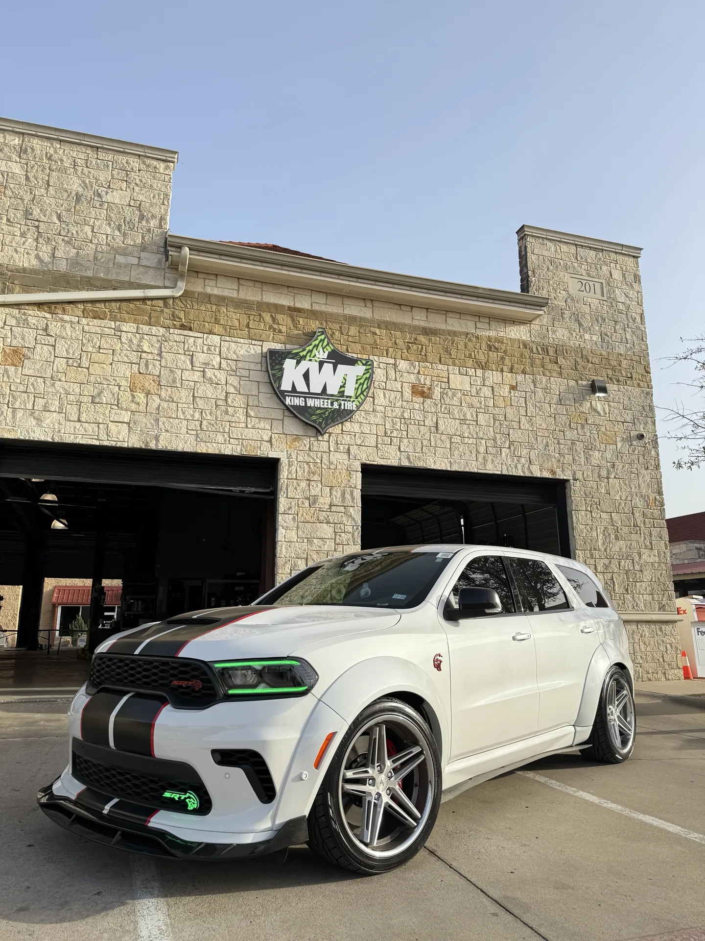A lowered white Dodge Durango SRT on polished wheels outside the shop